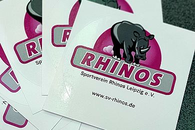 Aufkleber mit dem Logo des SV Rhinos Leipzig. Graues laufendes Nashorn in einem roten Halbkreis über dem Schriftzug RHINOS