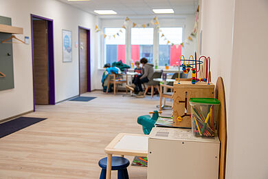 Blick in den Wartebereich, im Vordergrund Spielsachen für Kinder, im Hintergrund wartet ein Kind mit Elternteil