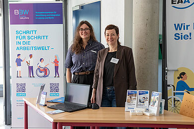 Zwei Frauen hinter einem Tisch mit Infomaterial zum Kompetenzzentrum und der EAA.