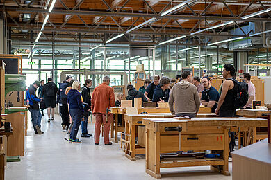 Viele Personen im Fachbereich Holztechnik. Die Gäste stehen verteilt zwischen Werkbänken und Arbeitstischen. 