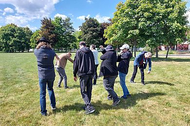 Gruppenarbeit beim Theatertreffen im Freien: Sieben Personen üben ein Stück ein. Sie tragen Jeans und Jacken.