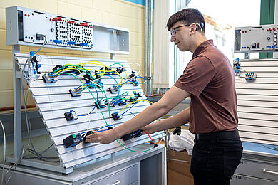 Ein Auszubildender steht an einer technischen Vorrichtung für Stromkreise.