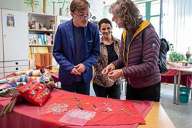 3 Personen stehen im Fachbereich Bekleidung an einem Tisch mit verschiedenen Produkten und unterhalten sich.