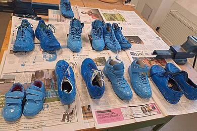 Auf einem Tisch, der mit Zeitung abgedeckt wurde, liegen blau bemalte Schuhpaare.