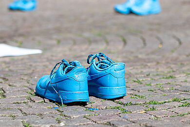 Mehrere Paare leuchtend blauer Schuhe stehen auf dem gepflasterten Boden.