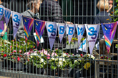 Fahne mit Schriftzug "35 Jahre BBW" an einem Gitterzaun. Im Hintergrund Pflanzen und mehrere Personen.