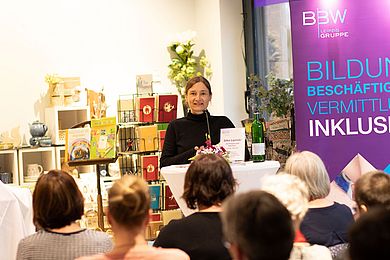Viele Menschen sind im Geschäft Nikolaieck. Autorin Silke Lipinski steht an einem Pult vor einem Mikrofon und liest aus ihrem Buch.