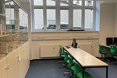 Bibliothek, links Schränke mit Büchern, rechts Tische mit grünen Drehstühlen